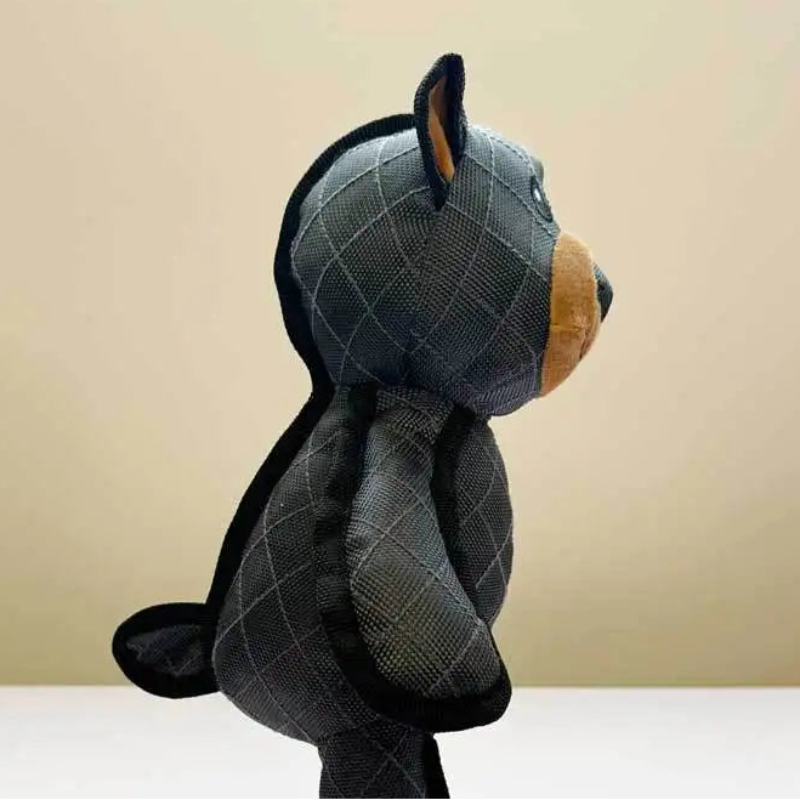 Plush toy resembling a bear fot a dog with a checkered pattern on a beige background